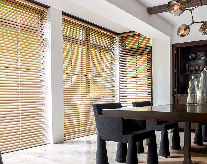 A dining room with floor to ceiling windows dressed with 2-inch Champagne Metal Blinds.