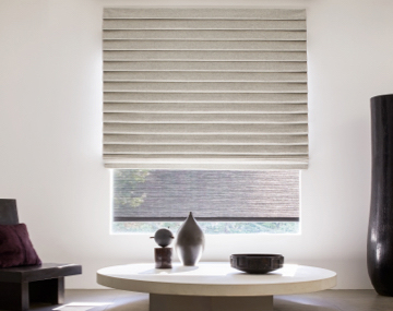 Pleated Roman Shade covers a large window in a room with a white table and black vase