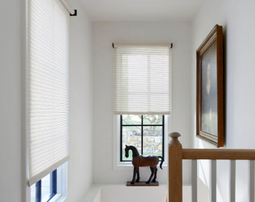 Roller Shades made of Mesa Verde cover windows in a stairwell with a wood railing and horse figurine