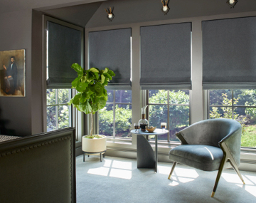 Flat Roman Shades hung over large windows in bedroom with monochromatic grey decor with chair and side table
