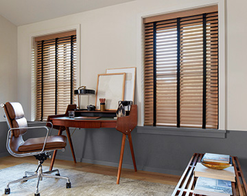 2 windows featuring Wood Blinds in 2 inch Oak in an office with a centered wooden desk, brown leather chair and wood bench