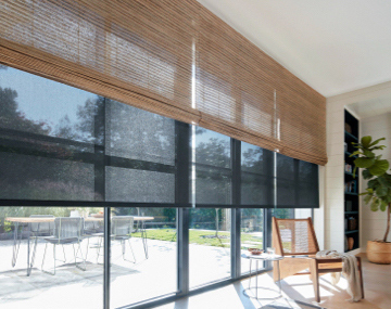 Waterfall Woven Wood Shades layered over Roller Shades cover floor to ceiling windows with patio furniture outside