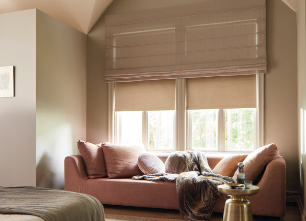 Two windows in a bedroom nook featuring Aventura Roman Shades in sheer elegance cocoa with a pink couch and fur blanket