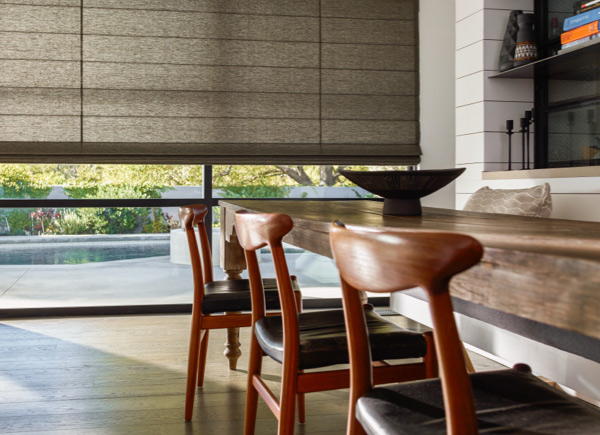 Large window featuring cascade woven wood shades in dakota charcoal hung in a dining room with a large wood table and chairs