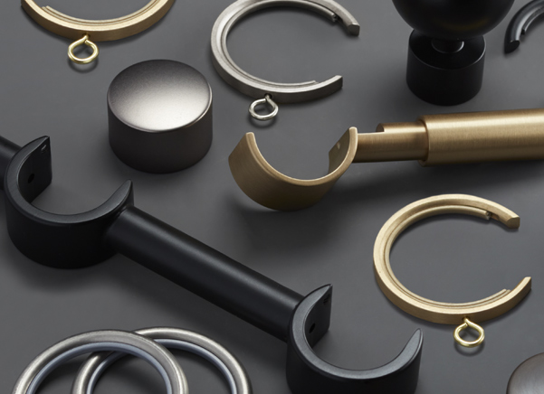 The components for the brass drapery hardware set Saratoga with innovative C-rings lay on a black table for dramatic effect