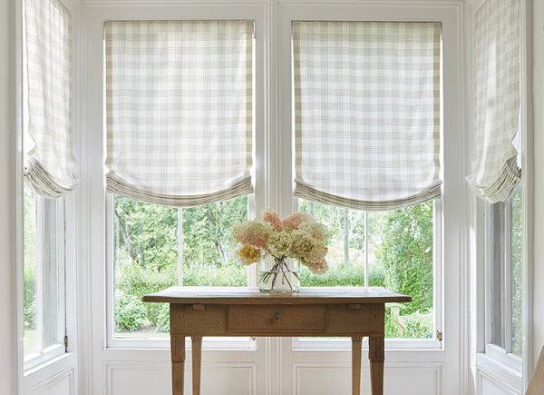 Four long windows featuring Relaxed Roman Shades in customers own material in an alcove with a small wooden table and flowers