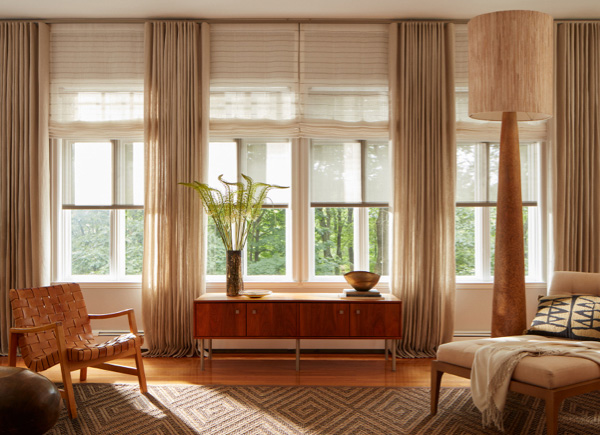 Four windows featuring ripple fold drapery in linen natural layered over solar shades and flat roman shades in a living room