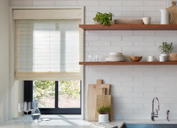 A window featuring standard woven wood shade in coastline muslin in a kitchen with white walls and wooden shelves over a sink